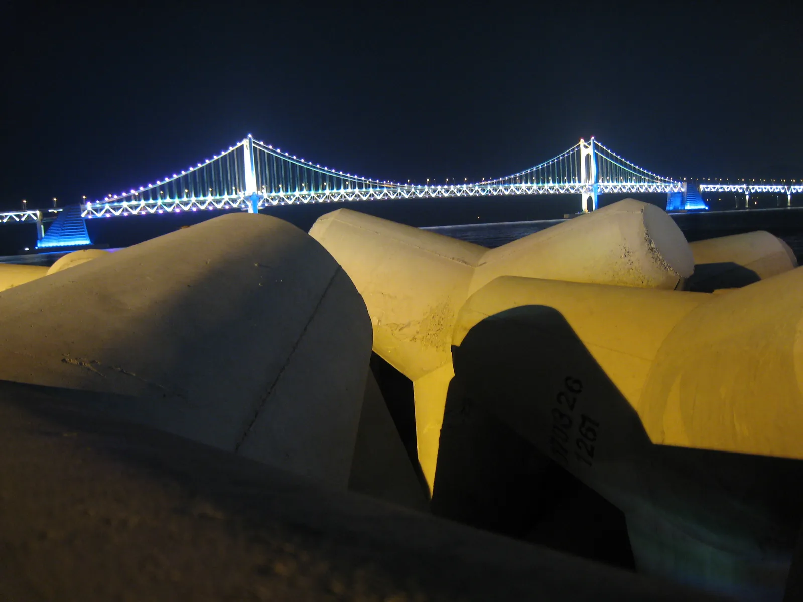 Gwangan Bridge lit up at night beyond the breakwater of a Busan harbour